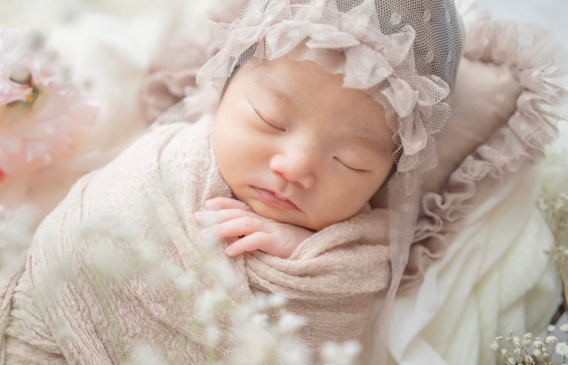レースのボンネットをかぶって眠る新生児